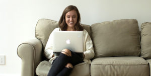 Meghan Easley, MAT Alumni, sitting on a couch with her laptop