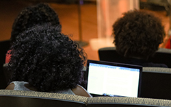 The back of a woman sitting in an auditorium audience